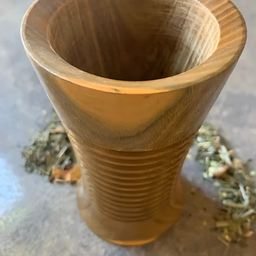 Kalebasse bauchig Rillen Palo Santo Holz Nahaufnahme mit losem Matetee im Hintergrund