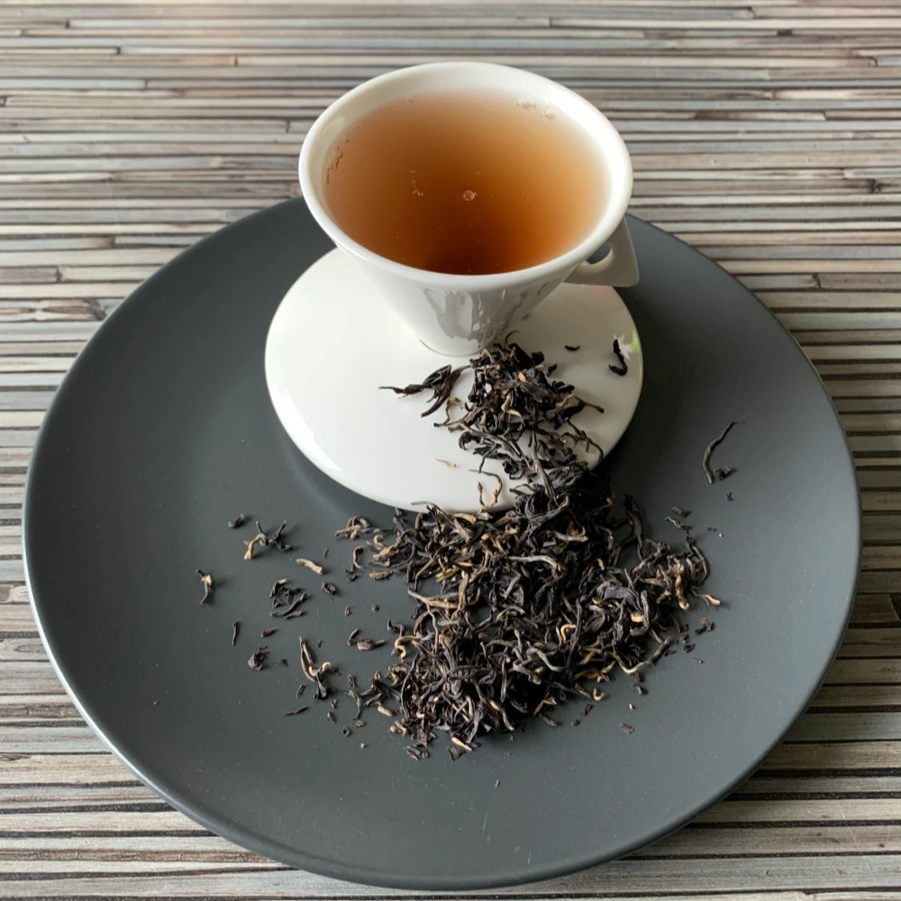 Kenia Tippy Purple Tea auf grauem Teller mit weißer Tasse vor gestreiftem Holzhintergrund