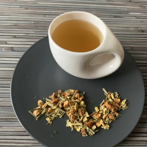 Kräutertee Cool Mint in weißer Tasse aufgegossen, lose Kräuter auf grauem Teller vor gestreiftem Holzhintergrund