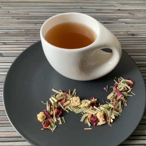 Kräutertee Fastenzeit ohne Aroma in weißer Tasse aufgegossen, lose Teemischung auf grauem Teller vor gestreiftem Holzhintergrund