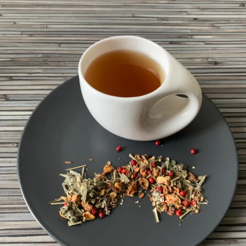 Kräutertee Faulenzer Mischung in weißer Tasse aufgegossen, lose Teemischung auf grauem Teller vor gestreiftem Holzhintergrund