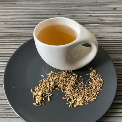 Kräutertee Fenchel Anis ohne Zusätze in weißer Tasse aufgegossen, lose Kräuter auf grauem Teller vor gestreiftem Holzhintergrund
