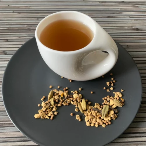 Kräutertee Kapha ohne Aroma Zusatz mit weißer Tasse auf grauem Teller vor gestreiftem Holzhintergrund