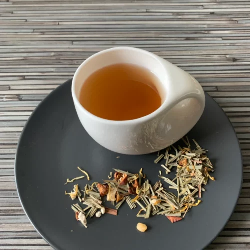 Kräutertee Lemongras Erdbeer aufgegossen in weißer Tasse, lose fruchtige Kräutermischung mit Zitronengras, Erdbeere, Ananas und Ringelblumen auf gestreiftem Holzhintergrund