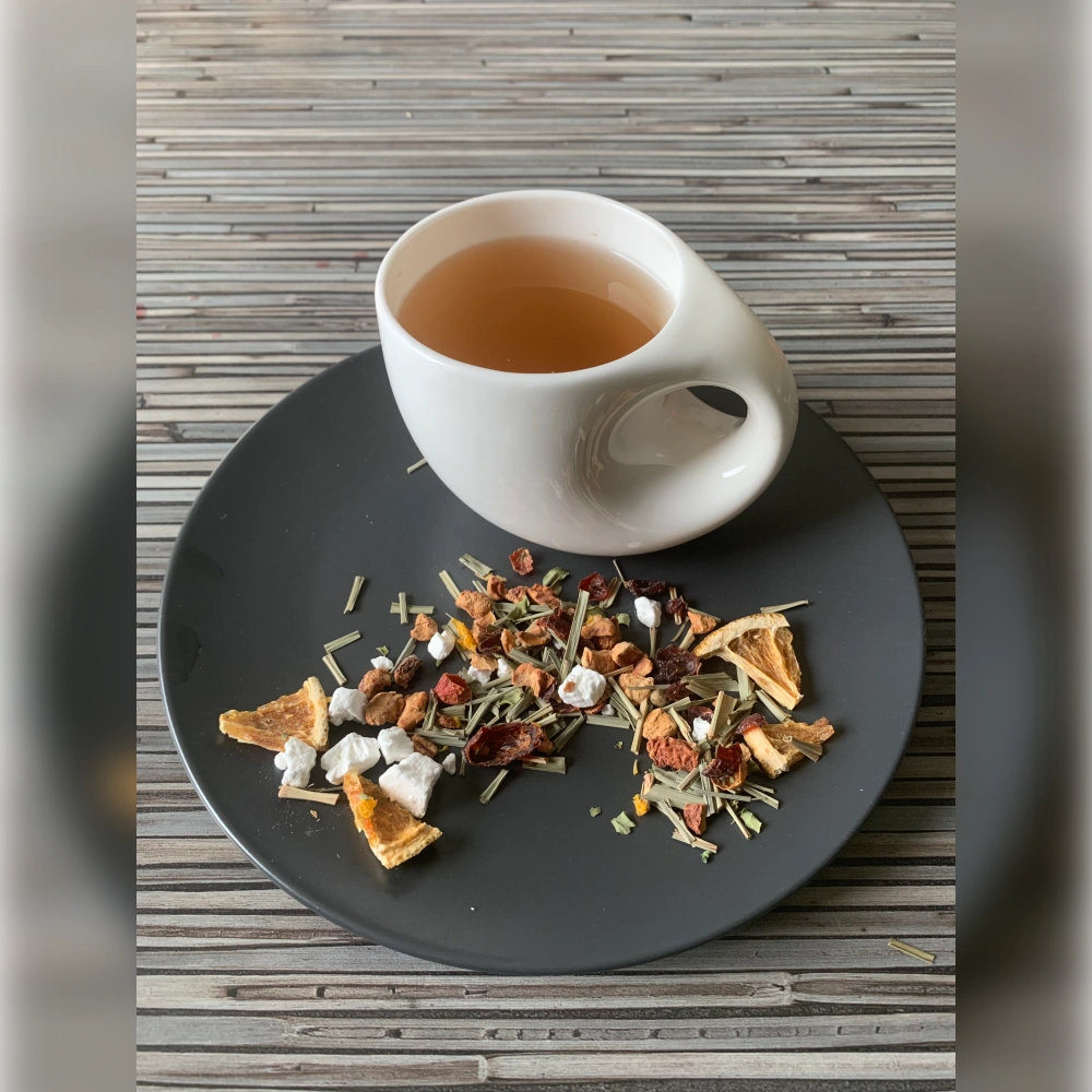 Kräutertee Moringa ohne Aromazusätze aufgegossen in weißer Tasse, lose Kräuterteemischung mit Moringablättern, Yuzu und Mandarinorange auf gestreiftem Holzhintergrund