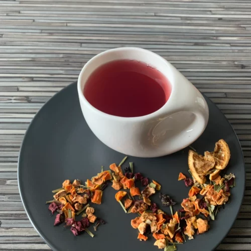 Kräutertee Orange Grapefruit aufgegossen in weißer Tasse, lose fruchtige Kräuterteemischung mit Orangen- und Hibiskusstücken auf gestreiftem Holzhintergrund