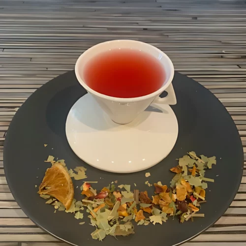 Kräutertee Oraya Mangoblätter aufgegossen in weißer Tasse, lose fruchtige Kräuterteemischung mit Mangoblättern, Orange und Hibiskus auf gestreiftem Holzhintergrund