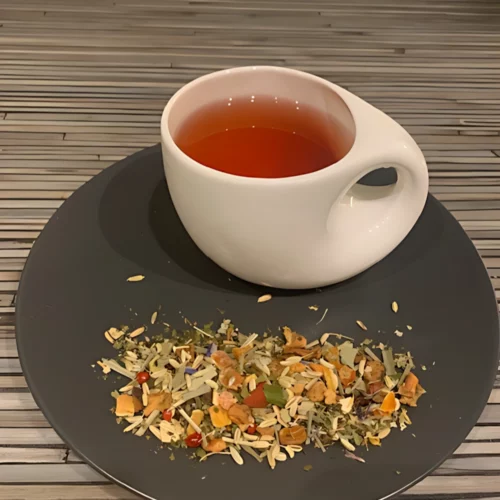 Kräutertee Relashio mit rötlicher Farbe, Fruchtstücken und Blüten in weißer Tasse, auf gestreiftem Holzhintergrund