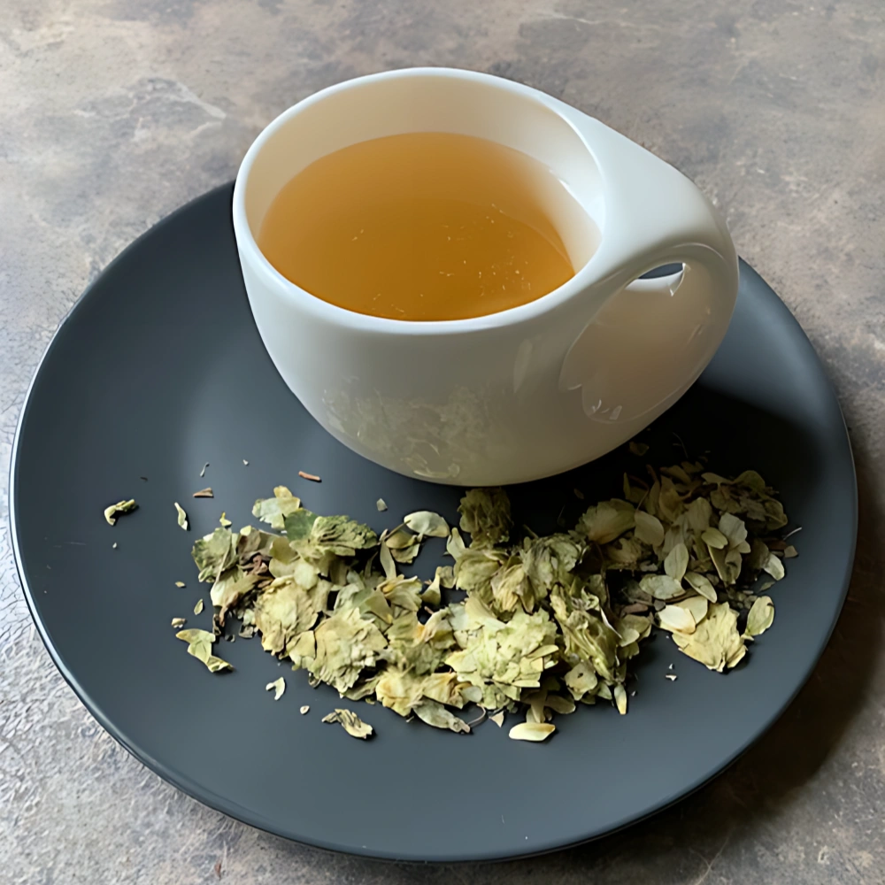 Kräutertee Zack und weg in weißer Tasse aufgegossen, lose Kräuterteemischung mit Hopfen und Melisse auf grauem Teller vor gestreiftem Holzhintergrund