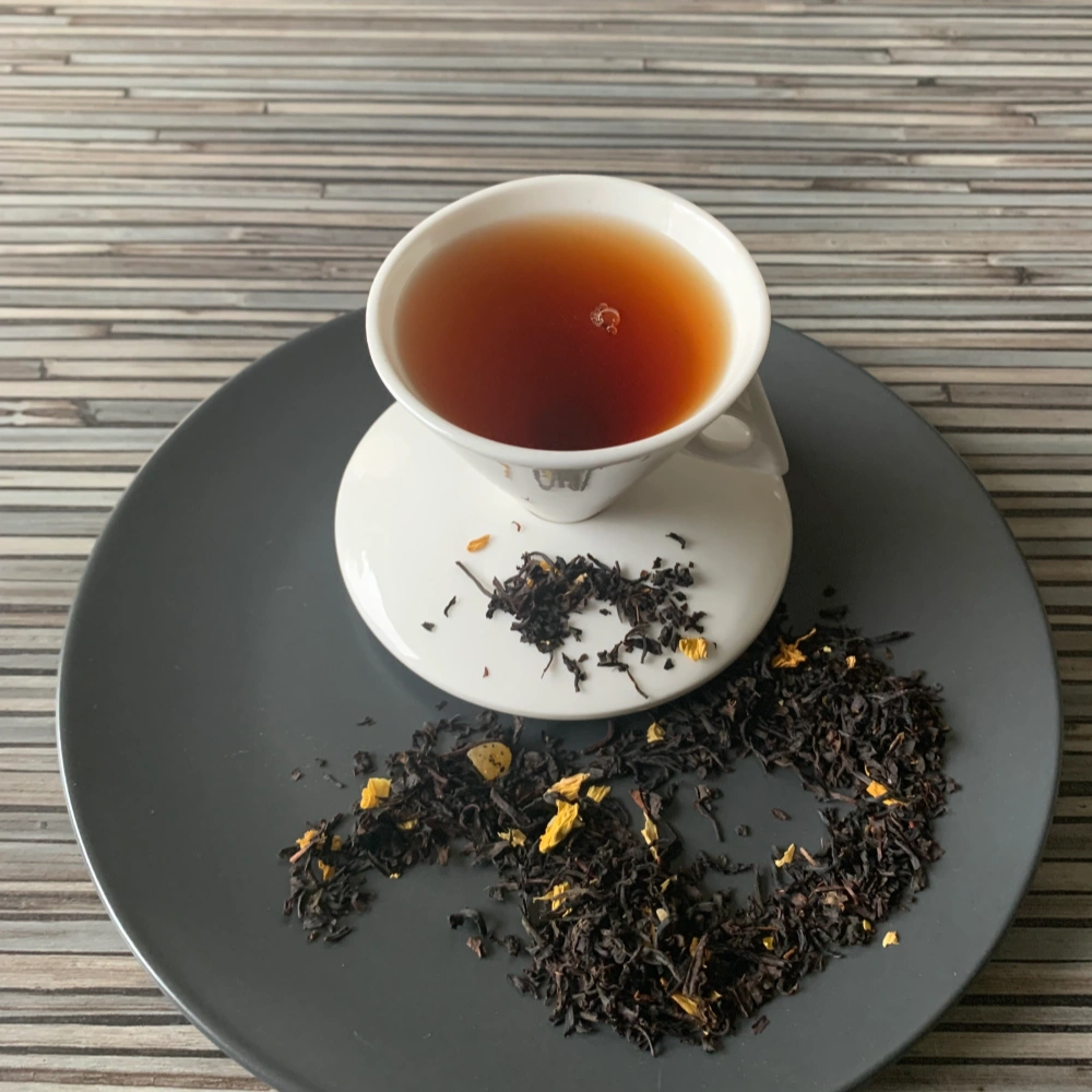 Schwarztee Mango mit Mangostücken und Blüten in weißer Tasse auf gestreiftem Untergrund