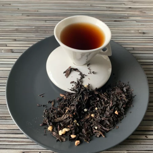 Maple Walnuss Ahorn halbfermentierte Oolong mit Teeblättern, Walnusskernen, Mandelstücken und heller, klarer Tassenfarbe in weißer Teetasse auf gestreiftem Hintergrund