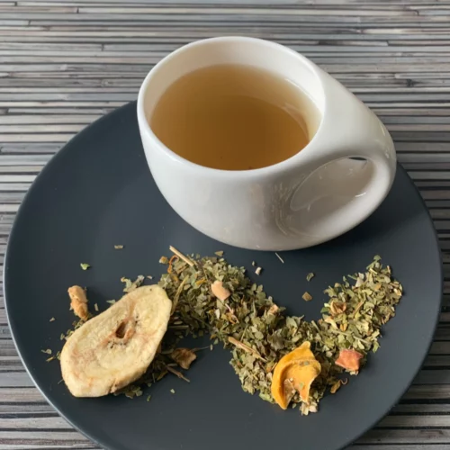 Kräutertee Mate Mexicano aufgegossen in weißer Tasse, lose Kräutermischung mit Mate, Mango, Banane, auf gestreiftem Holzhintergrund