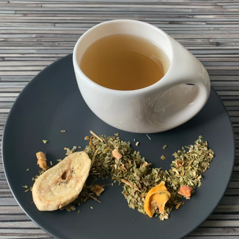 Kräutertee Mate Mexicano aufgegossen in weißer Tasse, lose Kräutermischung mit Mate, Mango, Banane, auf gestreiftem Holzhintergrund