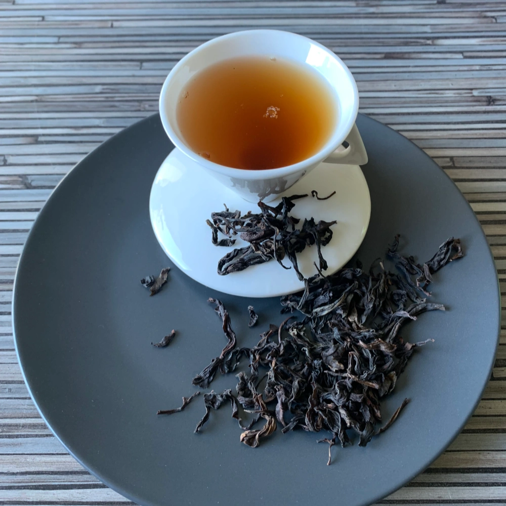 China Da Hong Pao Oolong mit großblättrigem Oolongtee und kupferfarbener Tassenfarbe in weißer Teetasse auf gestreiftem Holzhintergrund