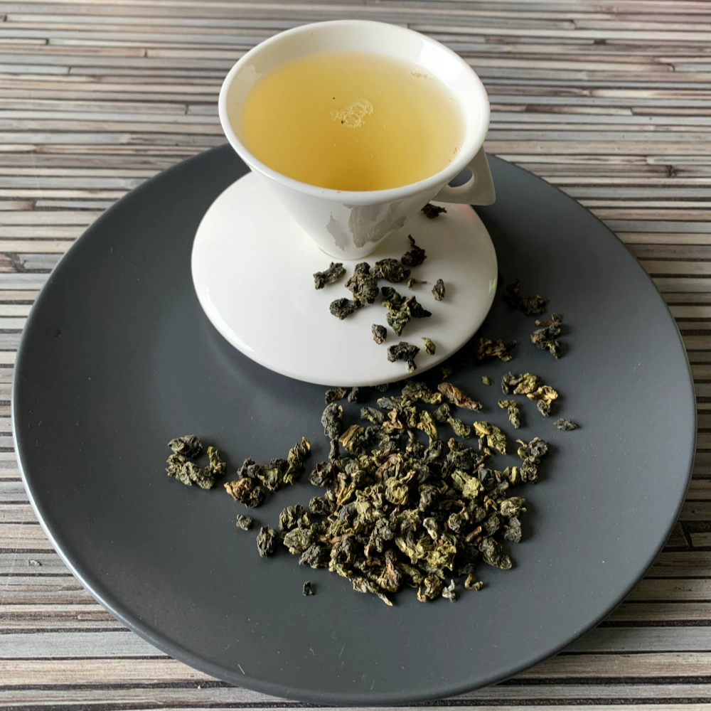 Formosa Classic Tung Ting Jade Oolong mit gerollten jadegrünen Oolongblättern und heller, bernsteinfarbener Tassenfarbe in weißer Teetasse auf gestreiftem Holzhintergrund