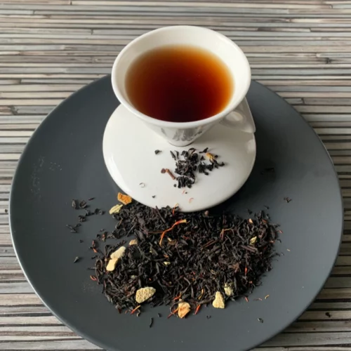Schwarztee Orange mit Schalen in weißer Tasse auf dunklem Teller auf gestreifter Holzplatte, loser Tee daneben