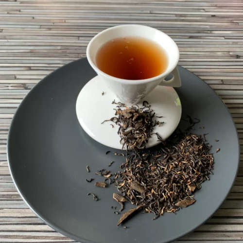 Ostfriesischer Sonntagstee mit Vanillestücken auf grauem Teller mit weißer Tasse vor gestreiftem Holzhintergrund