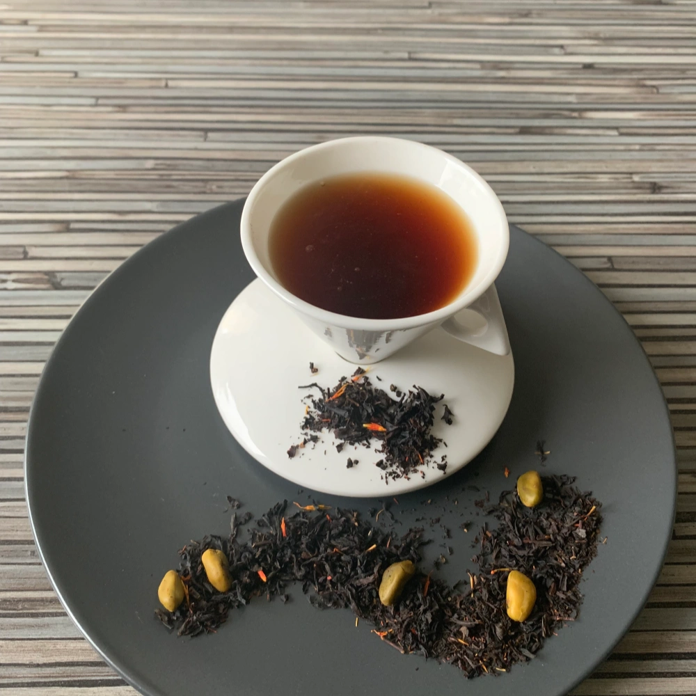 Schwarztee Pistazientrüffel in weißer Tasse auf dunklem Teller auf gestreifter Holzplatte, loser Tee mit Pistazien daneben