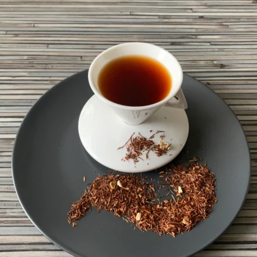 Rotbusch Earl Grey Bergamotte mit Rotbuschtee und Zitronenschalen und dunkler, klarer Tassenfarbe in weißer Teetasse auf gestreiftem Hintergrund