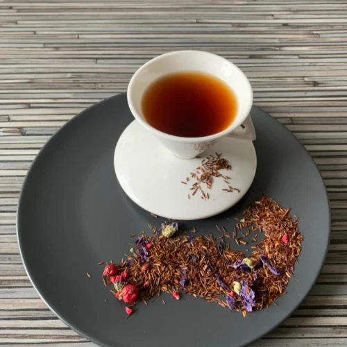 Rotbusch Granatapfel Traube Rooibos mit Blüten und Beeren, kupferfarbene Tassenfarbe in weißer Teetasse auf gestreiftem Hintergrund