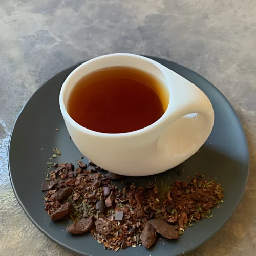 Rotbusch Kakao Vanille Schokominz mit Rotbuschtee und Kakaokernbruch, kupferfarbene Tassenfarbe in weißer Teetasse auf gestreiftem Hintergrund