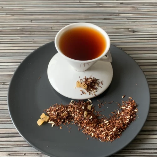 Rotbusch Piña Colada Kokos Ananas mit Rotbuschtee, Ananaswürfeln und Kokosraspeln, kupferfarbene Tassenfarbe in weißer Teetasse auf gestreiftem Hintergrund