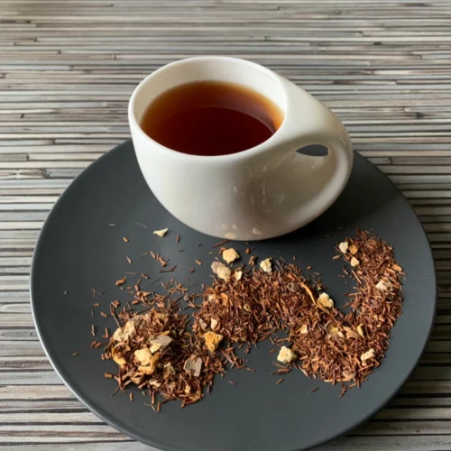 Rotbusch Schoko Orange in weißer Tasse, lose Teemischung mit Schokoladenplättchen und Orangenschalen im Teller auf gestreiftem Untergrund