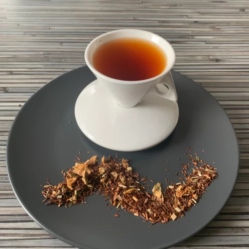 Rotbusch Zitrone Limette Tonka mit Rotbuschtee, Zitronenschalen und Zitronengras, helle Tassenfarbe in weißer Teetasse auf gestreiftem Hintergrund