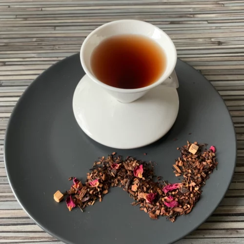 Schokotorte Honeybuschtee angerichtet auf Teller, darauf eine weiße Tasse mit eingeschenktem Tee.