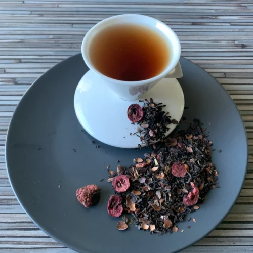 Schwarztee Skandinavische Sehnsucht in weißer Tasse auf dunklem Teller auf gestreifter Holzplatte, loser Tee mit