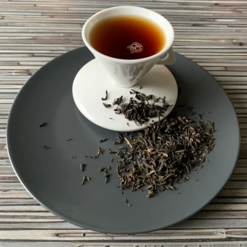 Vietnam Golden Tippy OP auf grauem Teller mit weißer Tasse vor gestreiftem Holzhintergrund