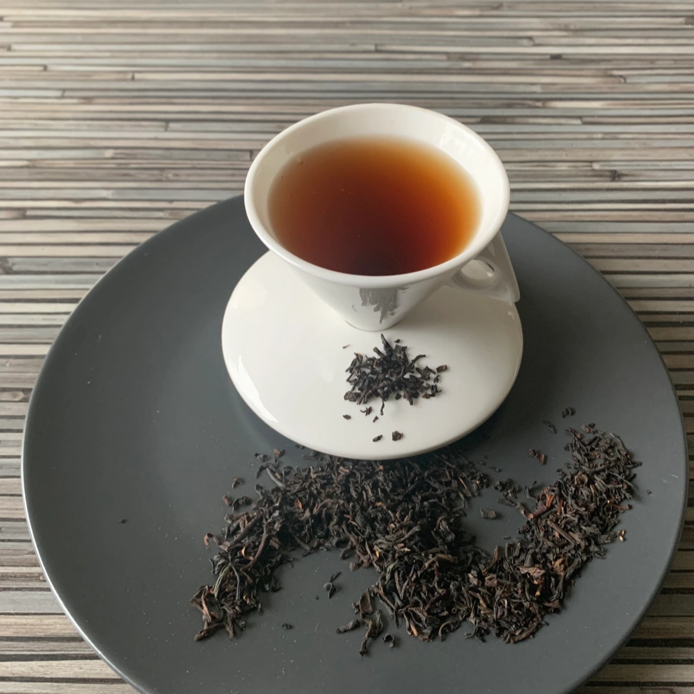 Schwarztee Wildkirsch – Kirschtee in weißer Tasse auf dunklem Teller auf gestreifter Holzplatte, loser Tee