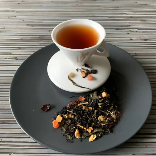 Schwarztee Zartes Bussi in weißer Tasse auf dunklem Teller auf gestreifter Holzplatte, loser Tee mit Blüten und Fruchtstücken daneben