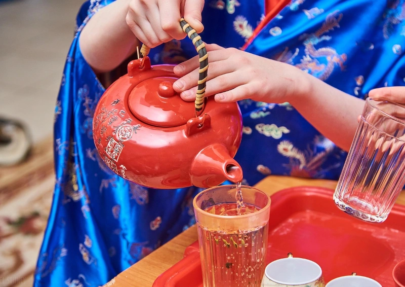 China Schwarztee wird aus roter Teekanne in Glas gegossen.