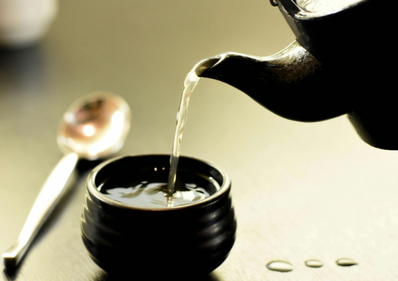 Grüntee Fei Cui wird aus einer schwarzen Kanne eingeschenkt.