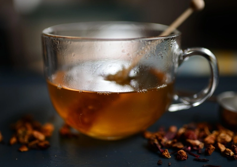 Winterlicher Kräutertee mit Honig in Glastasse auf dunklem Hintergrund.