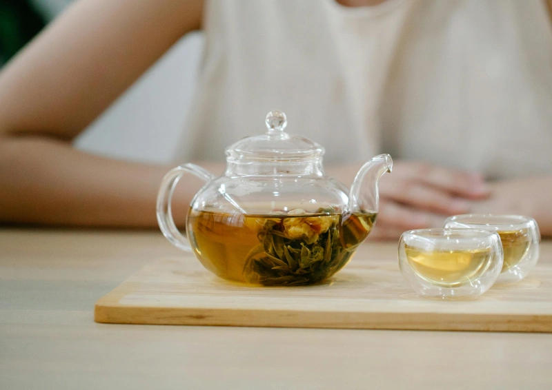 gruener tee in teekanne mit tasse frau im hintergrund