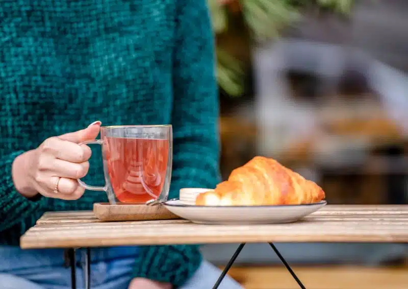 Frau im französischen Teehaus im Freien mit Tee und Croissant