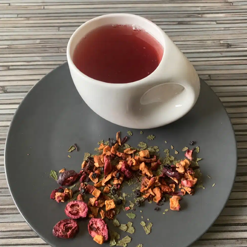 Früchtetee Moringa Berry Balance in weißer Tasse auf grauem Teller vor gestreiftem Holzhintergrund