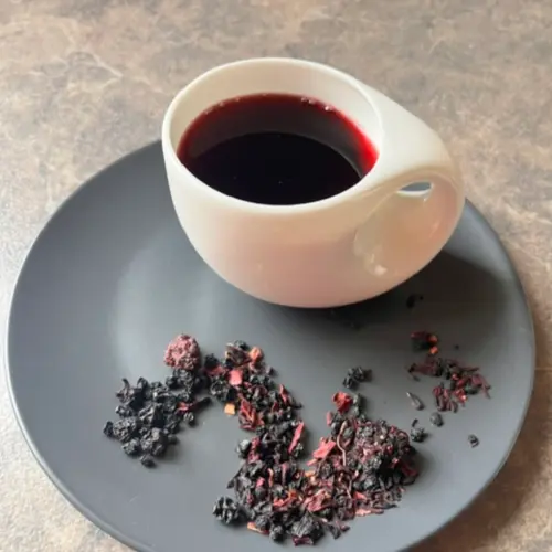 Früchtetee Bragis Becher lose auf grauem Teller und aufgegossen in weißer Tasse